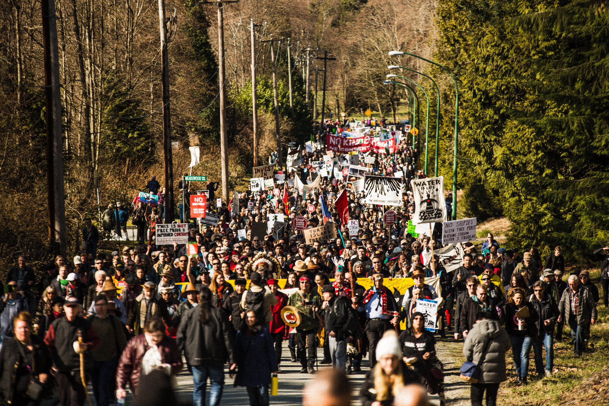 Large crowd marching with signs and banners opposing Trans Mountain